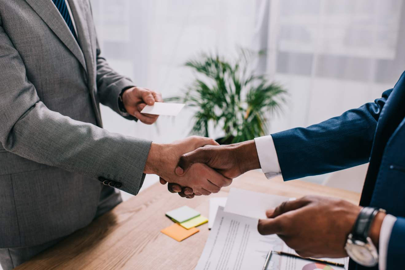 Cropped image of two businessmen shaking hands and giving visit cards to each other